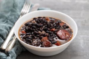 black beans with meat and sausages in white bowl on ceramic background