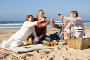four-senior-friends-having-picnic-beach-sunny-day-raising-glasses-red-wine-pronouncing-toast-two-middle-aged-couples-clinking-glasses-celebrating-outside-celebration-leisure-concept