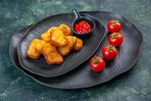 delicious-chicken-nuggets-ketchup-tomatoes-black-plates-dark-surface-with-free-space
