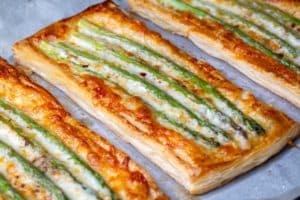baked-green-asparagus-with-ham-cheese-puff-pastry-sprinkled-with-sesame-seeds-green-basil-leaves_693630-111