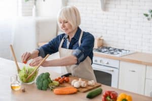 cheerful-old-senior-elderly-aged-woman-adding-tomatoes-vegetable-salad-fresh-ingredients